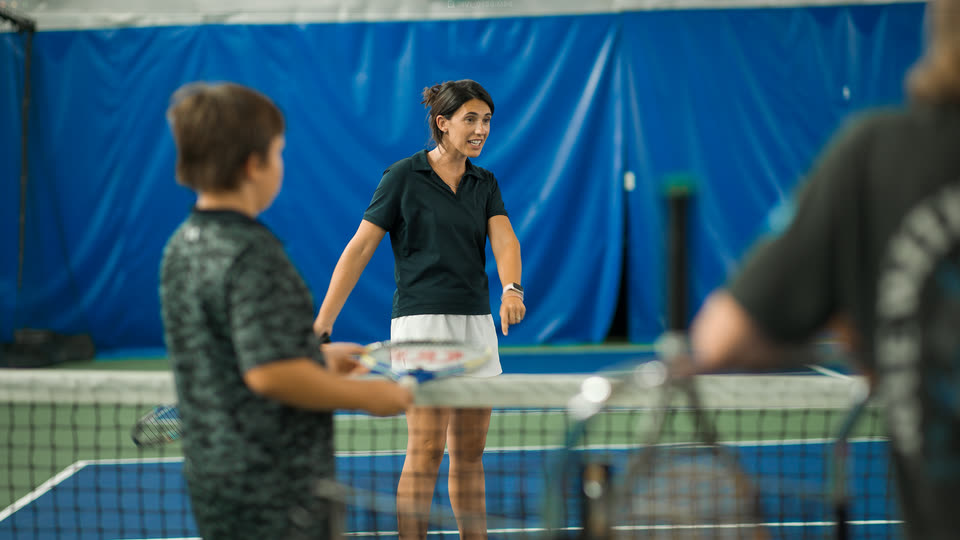 A coach talking with a junior player at the net at Match Point KC