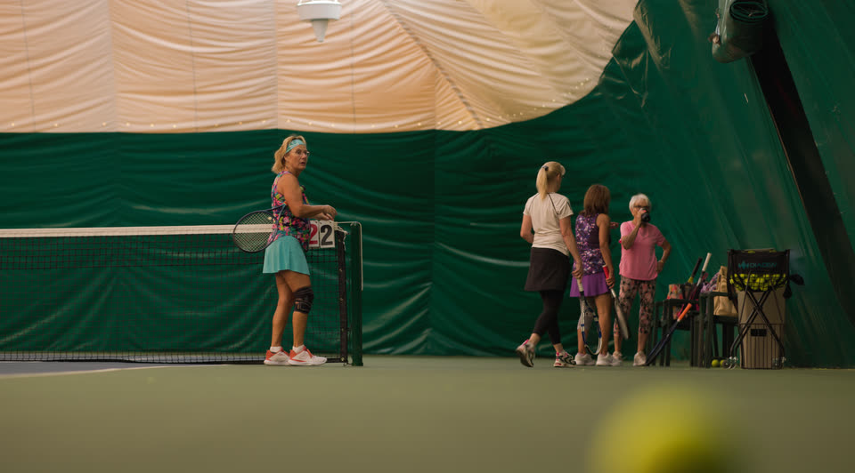 A women's group session gathered at the net with a coach at Match Point KC