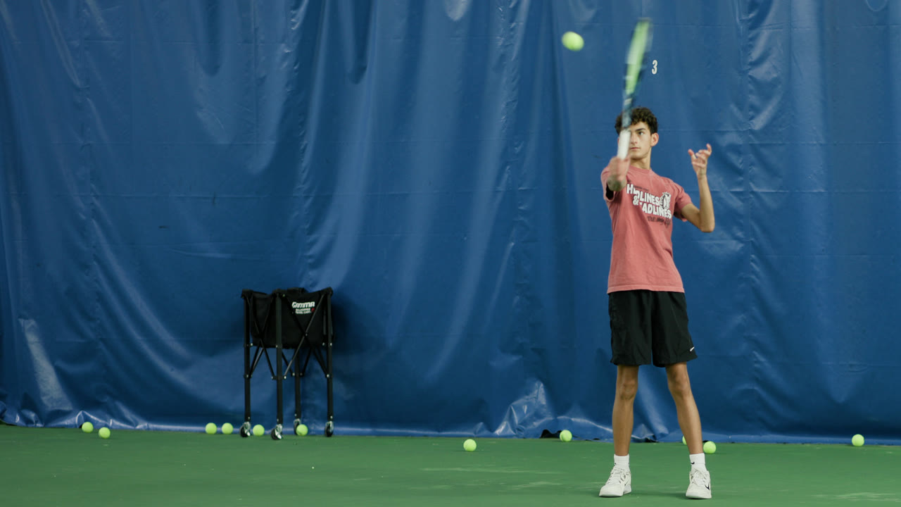 A junior player tossing the ball to serve on an indoor court at Match Point KC