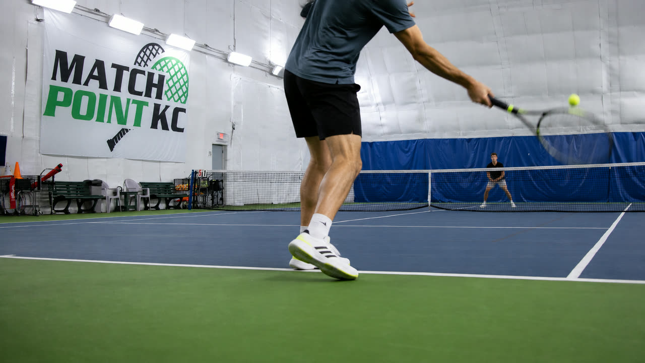 A player hitting a forehand in front of the Match Point KC wall sign